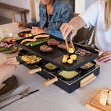 People using a raclette grill with various foods on a dining table.